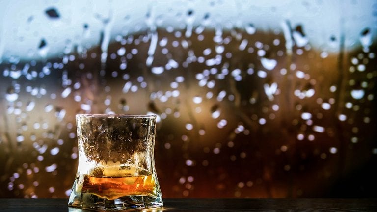 Glass of whiskey with rainy background